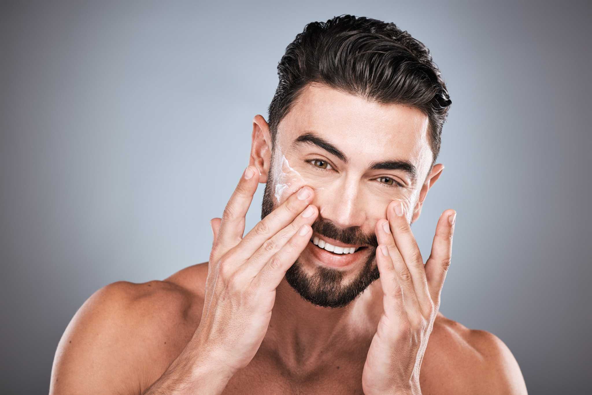 Smiling man gently massaging anti-aging face cream into his skin, highlighting daily skincare for men.