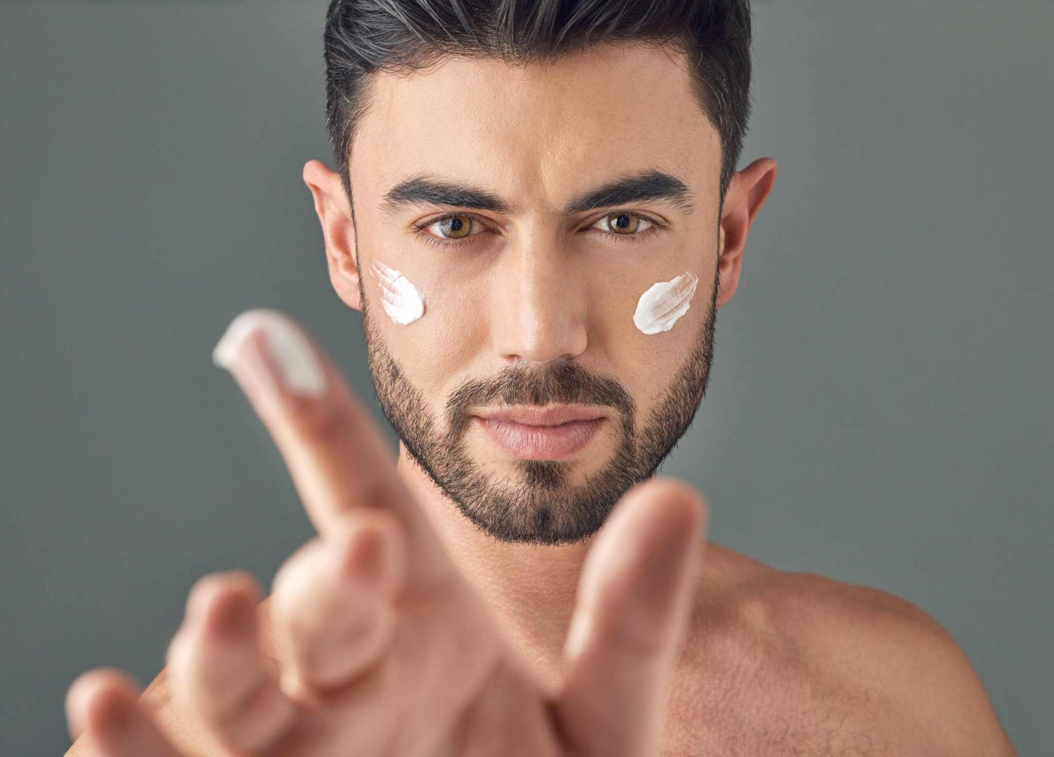 Focused man with cream dots on his cheeks, ready to apply anti-aging moisturizer as part of his morning skincare routine.