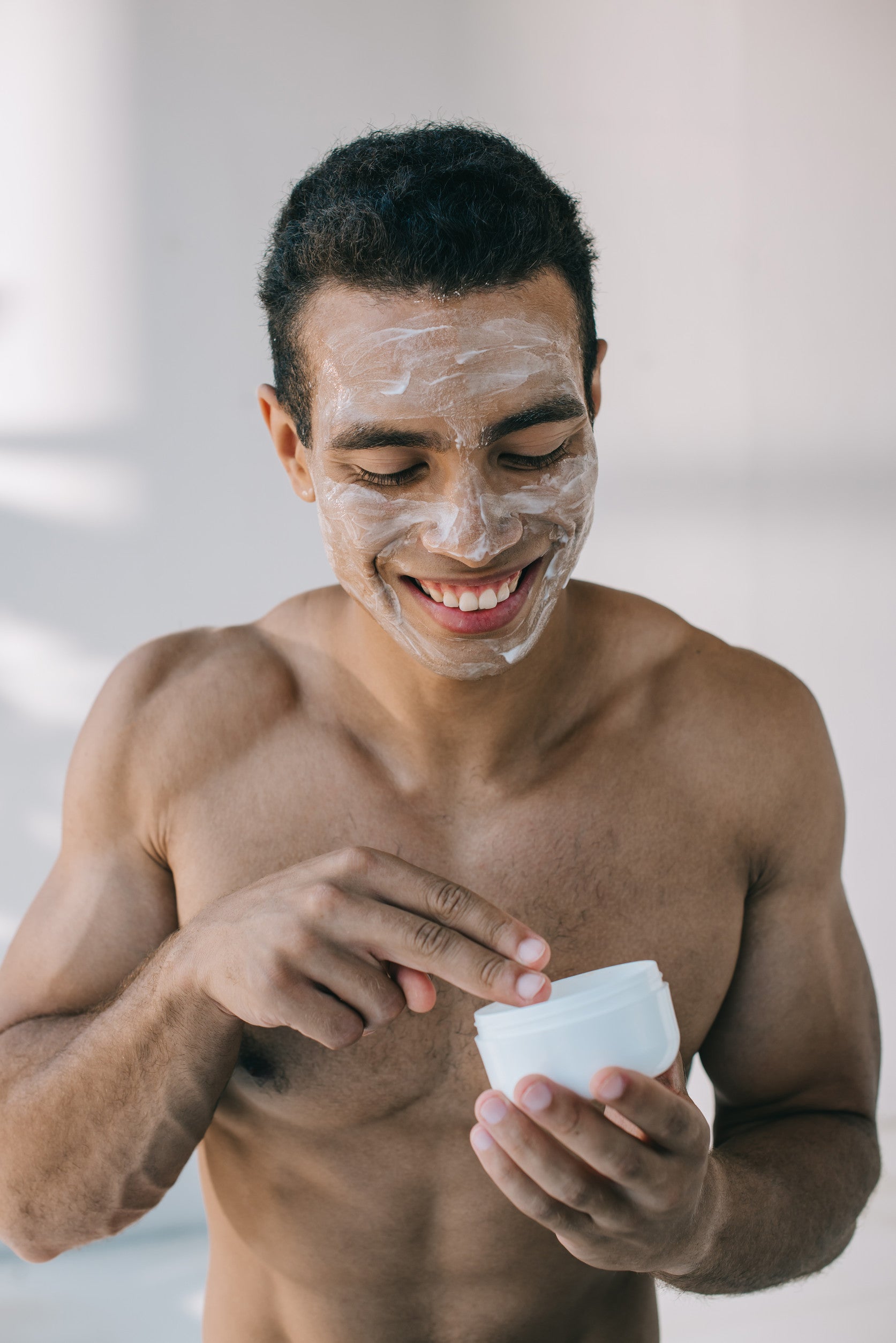 Man smiling while applying VMEN’S Icelandic Volcano AHA Scrub to his face in a natural light setting.