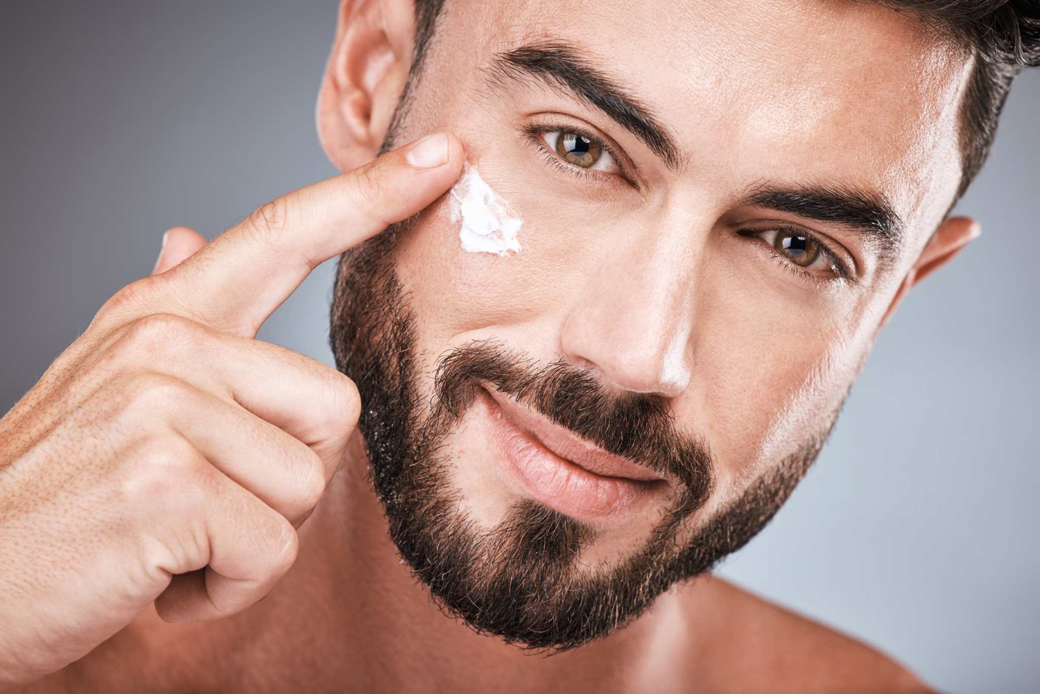Close-up of a man applying anti-age day cream to his cheek, showcasing smooth, healthy skin and a confident grooming routine.