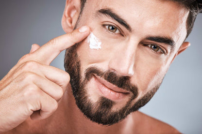 Close-up of a man applying anti-age day cream to his cheek, showcasing smooth, healthy skin and a confident grooming routine.