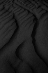 Aesthetic backdrop of fine black sand highlighting the volcanic inspiration behind the product., vmen&