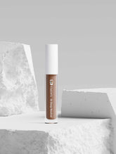Correcting Concealer for Men in shade 35 Deep Neutral, in a clear tube with a white cap, positioned on textured white blocks.