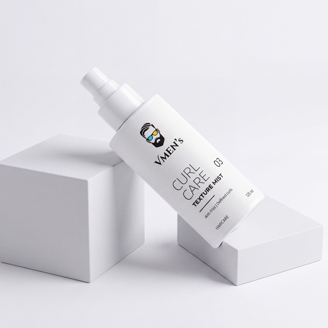 VMEN’S Anti-Frizz Curly Hair Texture Mist for Men spray bottle resting diagonally across white display blocks.