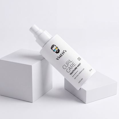 VMEN’S Anti-Frizz Curly Hair Texture Mist for Men spray bottle resting diagonally across white display blocks.