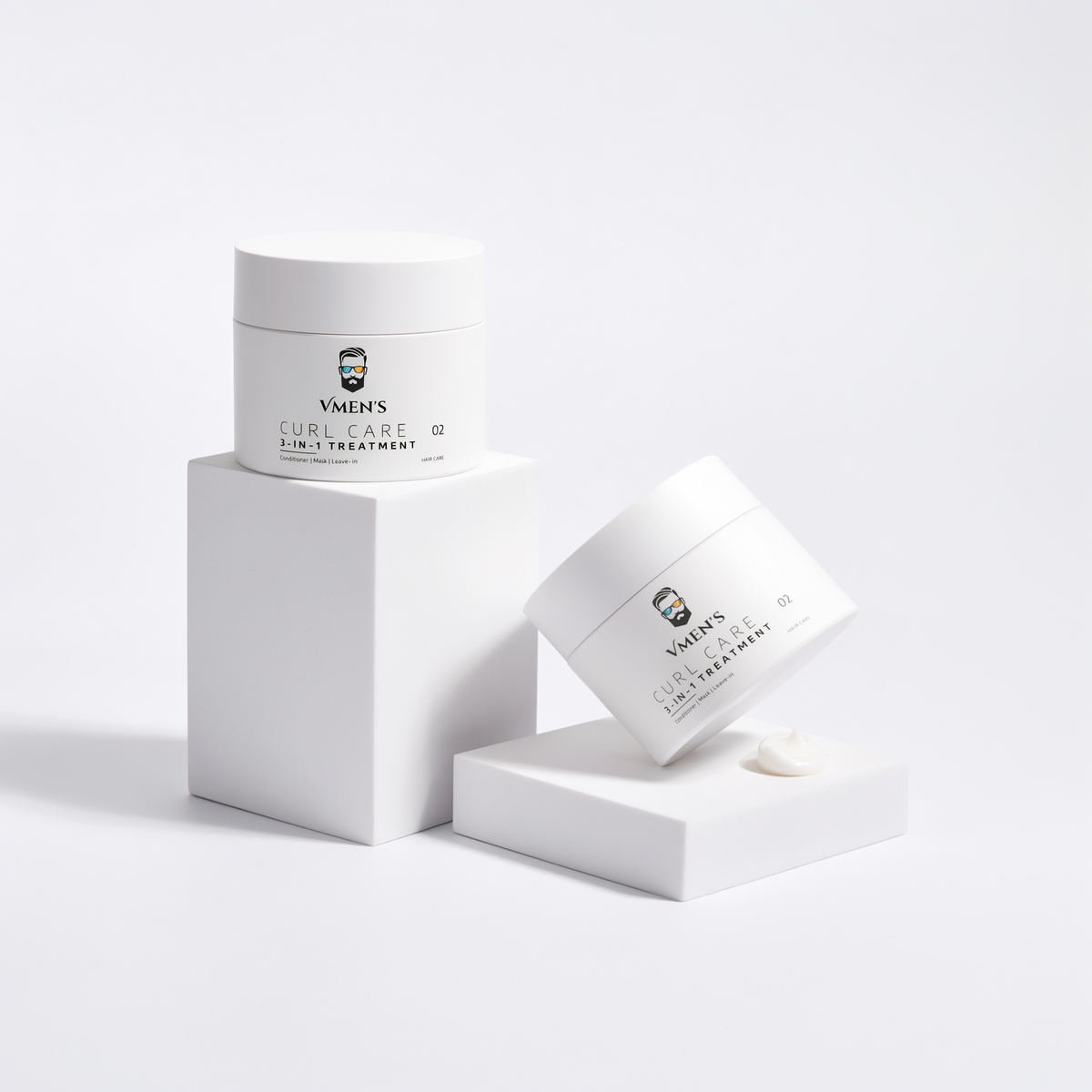 Two VMEN’S 3-in-1 Curly Hair Treatment for Men jars on white display blocks beside a small cream swatch.